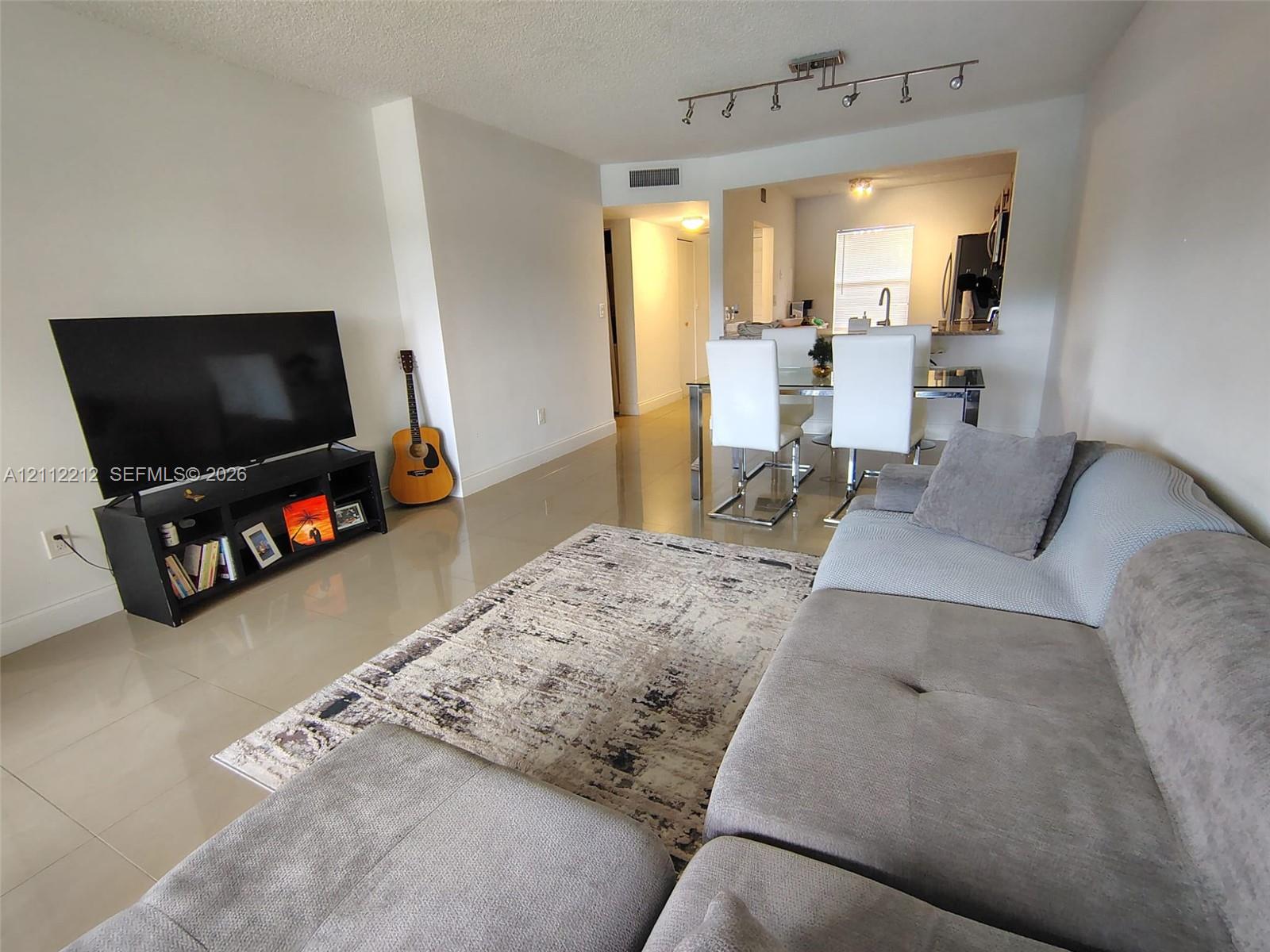 Open-concept interior featuring large-format tile flooring, recessed track lighting, and a kitchen pass-through window with an integrated breakfast bar