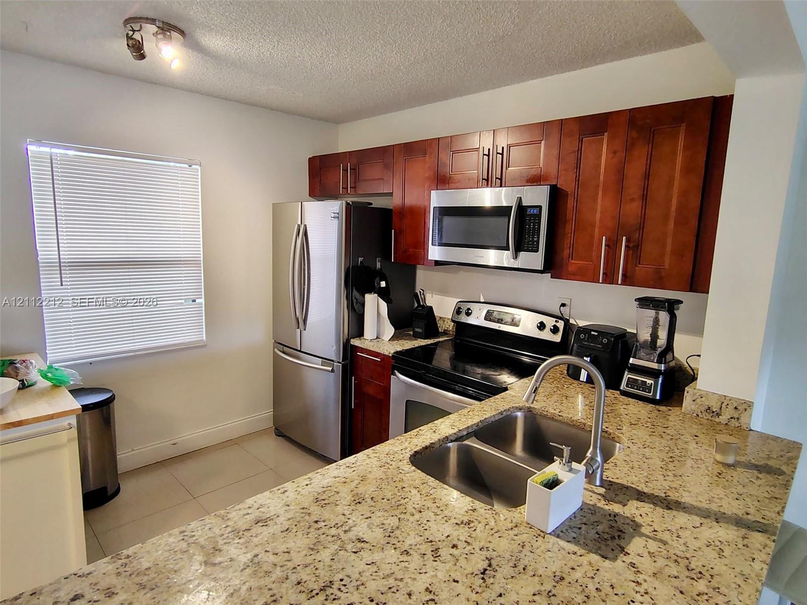 Kitchen featuring cherry-finish cabinetry, stone countertops, stainless steel appliances, and a dual-basin undermount sink with a high-arch faucet