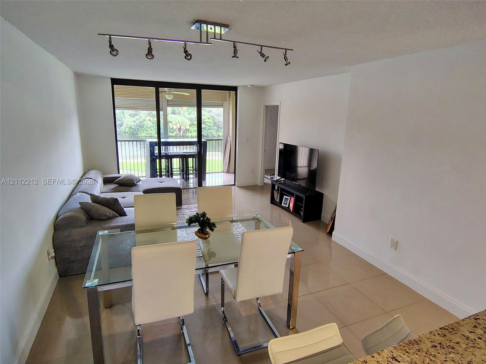 Open-concept floor plan with large-format tile flooring, multi-directional ceiling track lighting, and full-height sliding glass doors leading to a screened balcony