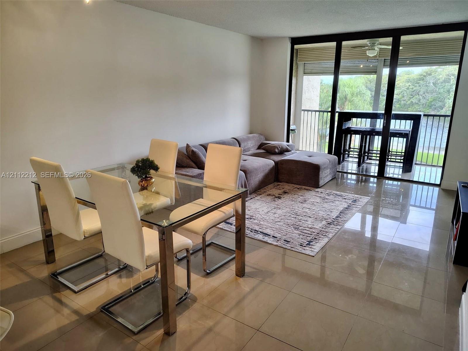 Living area featuring large-format tile flooring, floor-to-ceiling glass sliding doors, and a screened balcony with metal railing