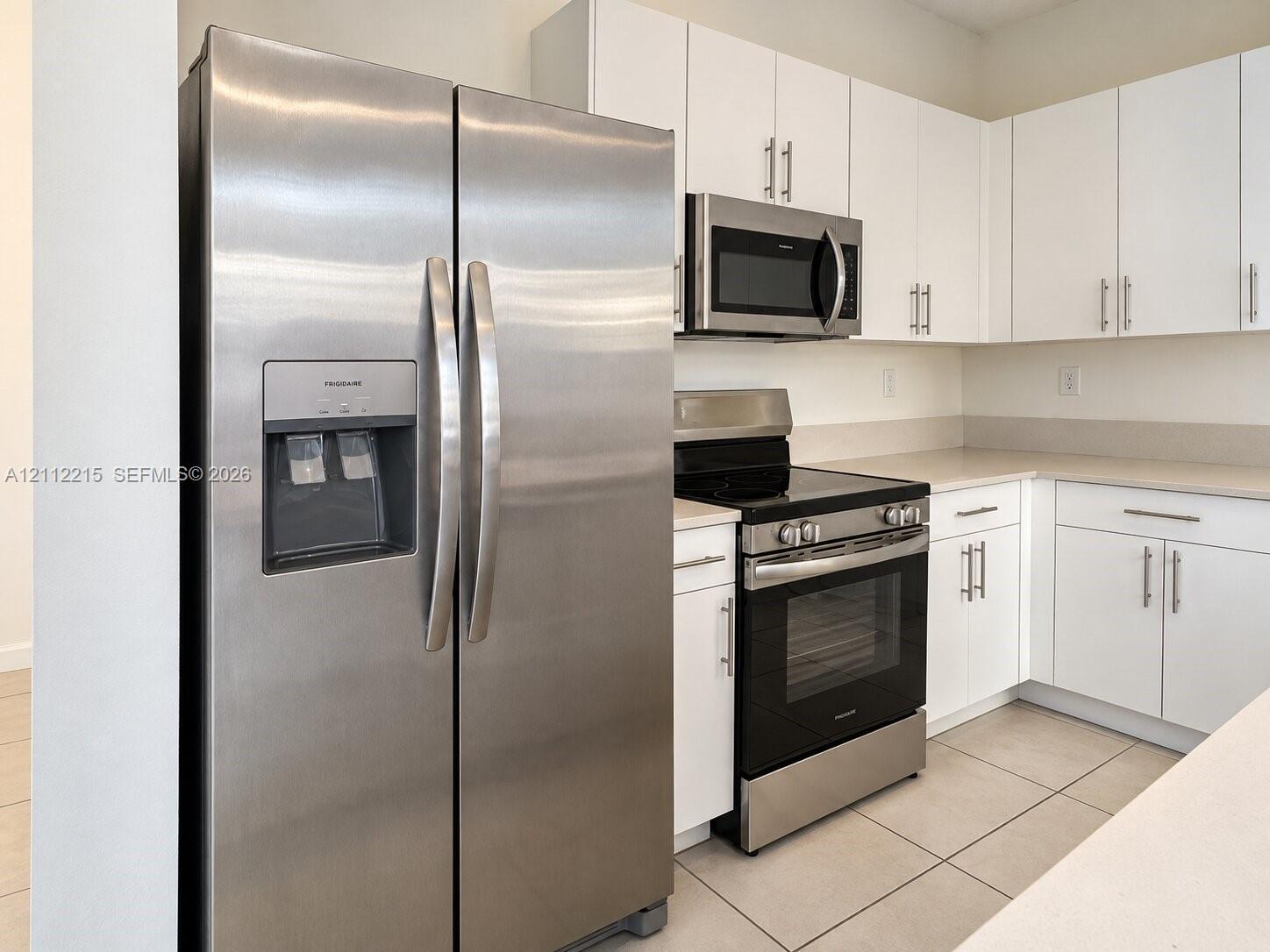 Kitchen featuring white cabinetry with brushed metal hardware, stainless steel side-by-side refrigerator, matching microwave, black range, and tile flooring