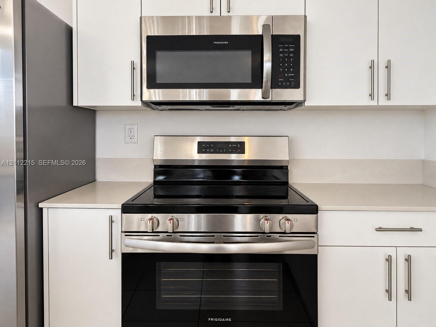 Stainless steel electric range and matching over-the-range microwave, crisp white cabinetry with modern pulls, and light-toned solid surface countertops