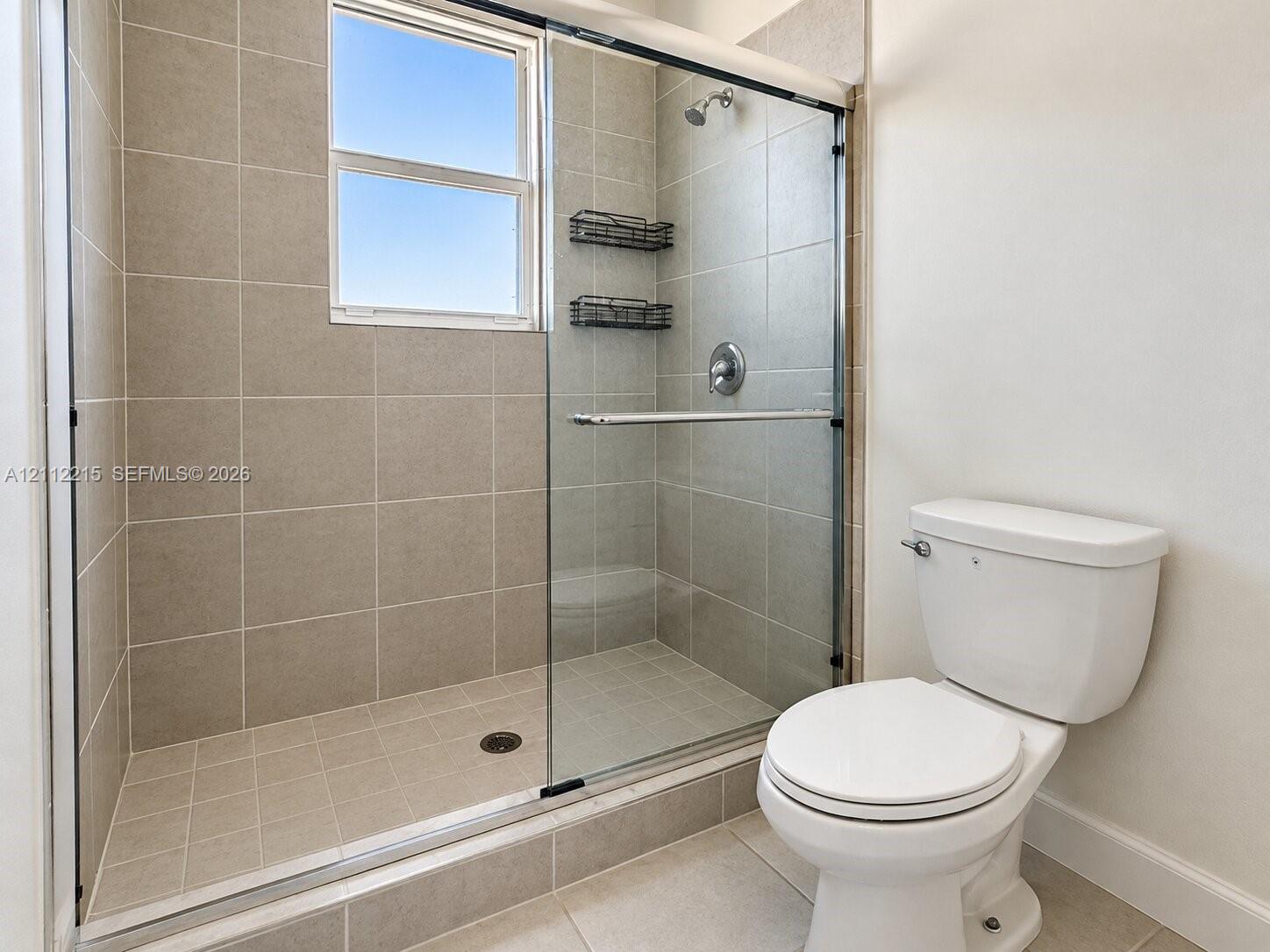 Walk-in shower enclosure featuring floor-to-ceiling tile, a sliding glass door, a window, and a wall-mounted showerhead