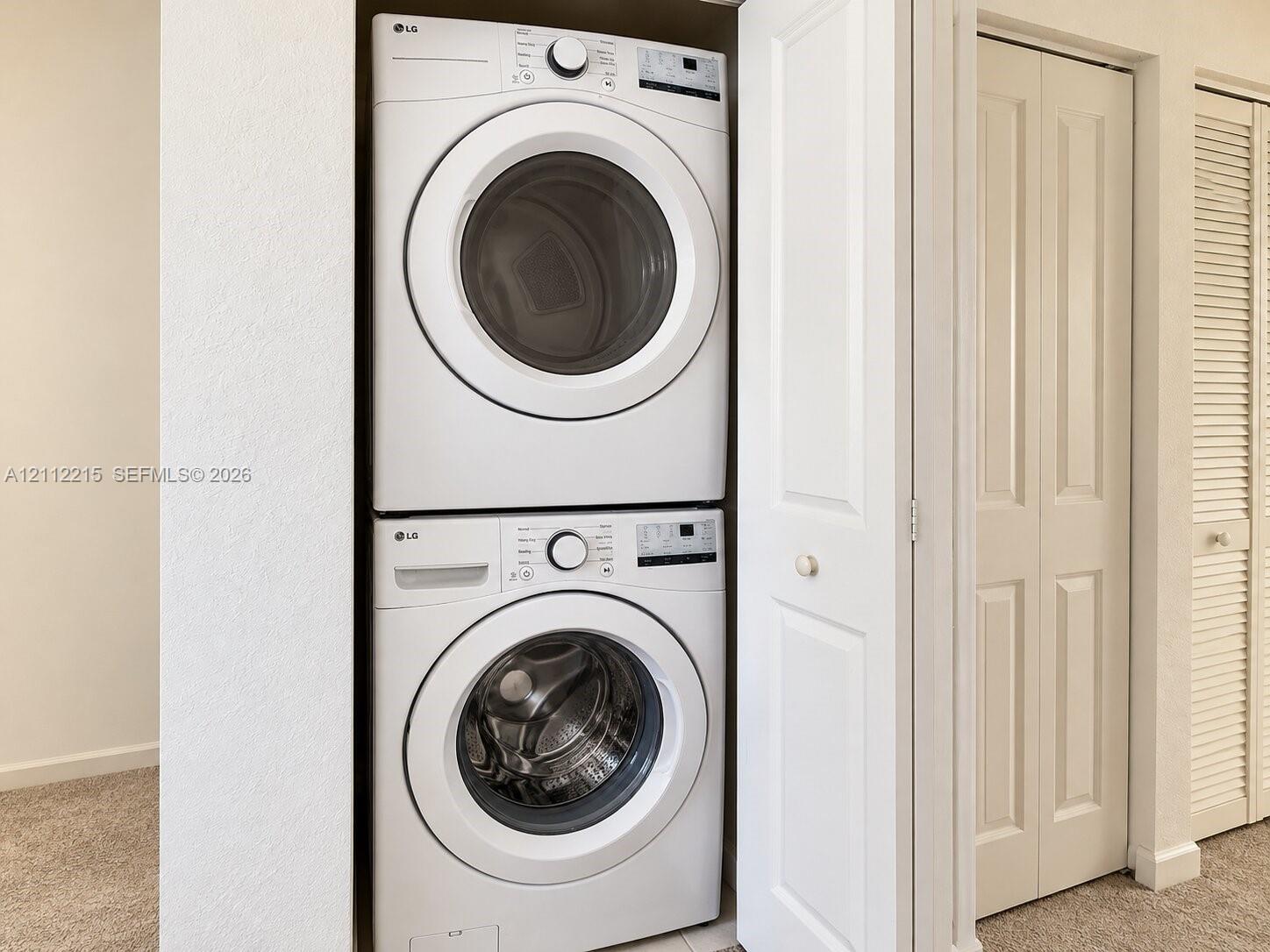 Stacked front-loading washer and dryer unit housed within a dedicated closet featuring bifold doors