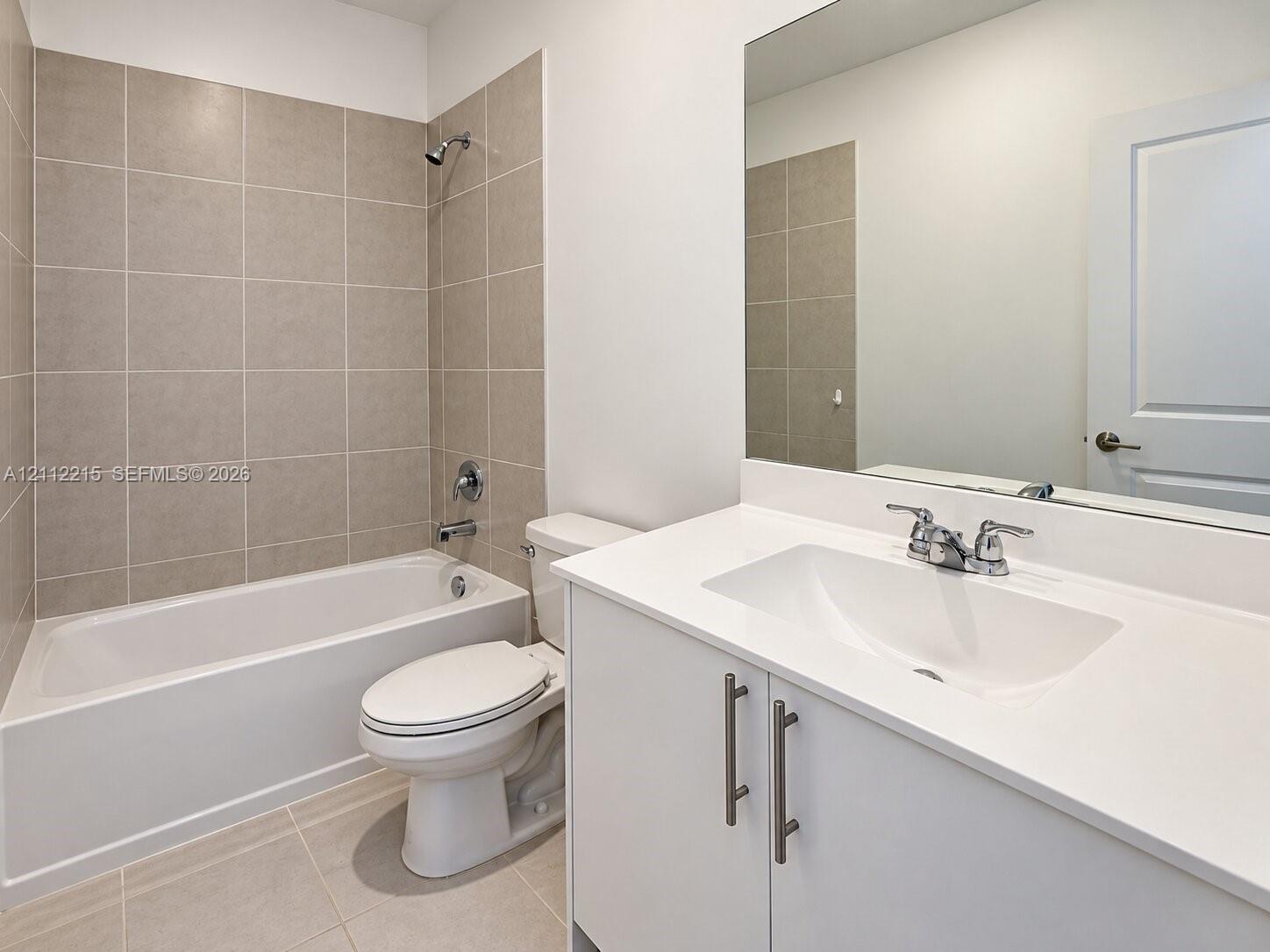 Bathroom featuring a white vanity cabinet with quartz countertop, integrated sink, polished chrome faucet, large wall-mounted mirror, and a tub-shower combination with floor-to-ceiling tile surround