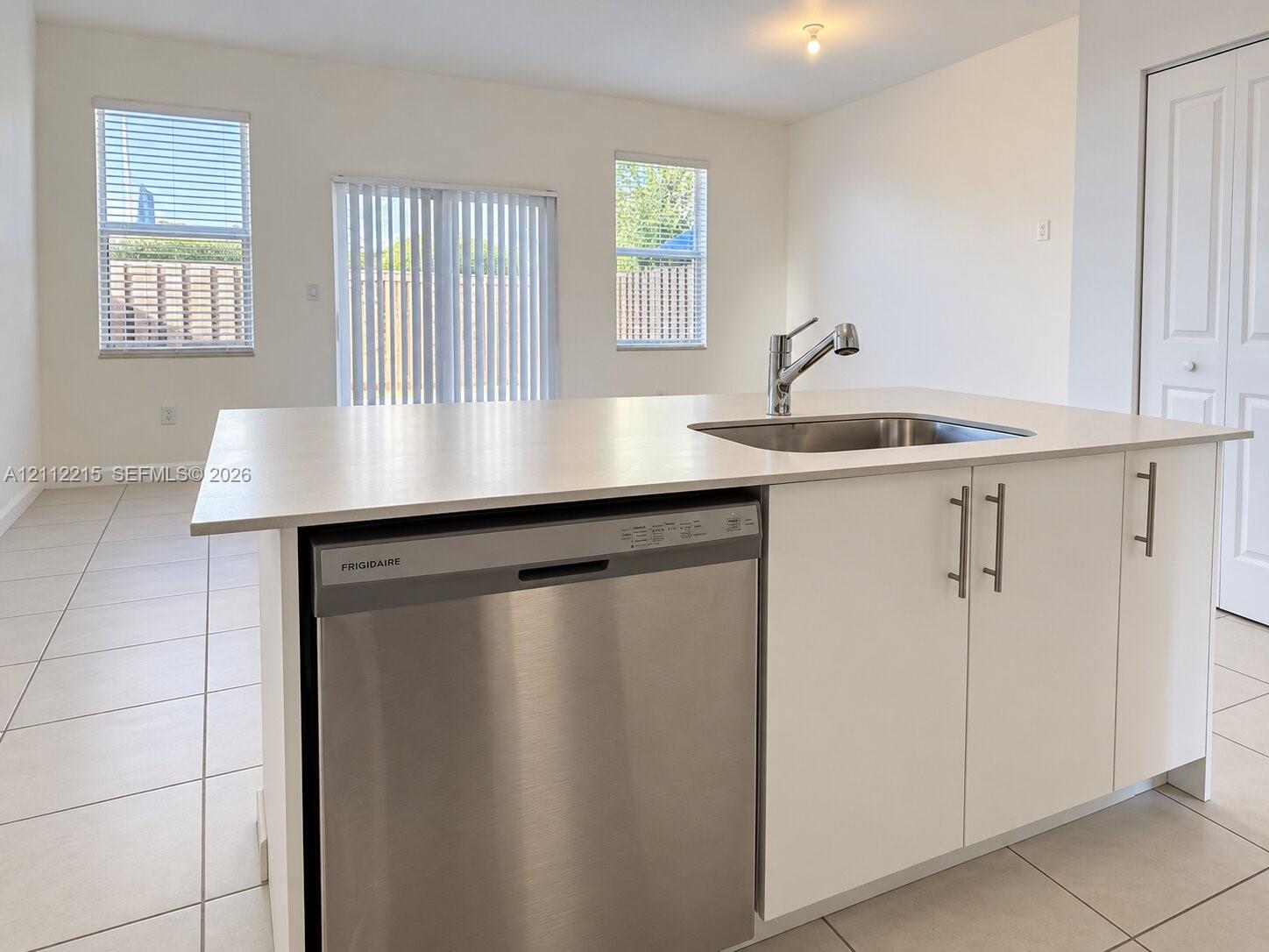 Kitchen island featuring a stainless steel dishwasher, an undermount sink with a high-arch faucet, white cabinetry, and light-toned countertops