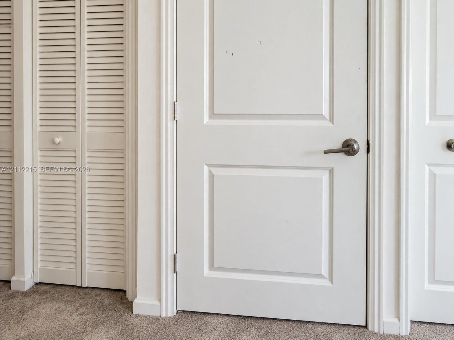 Interior featuring white two-panel solid core doors, white louvered bifold closet doors, and brushed nickel lever-style door hardware