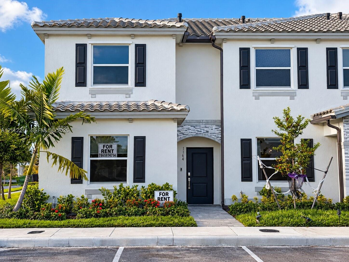 Two-story stucco exterior featuring a tiled roof, decorative shutter accents, stone-veneered entryway arch, and paved walkway