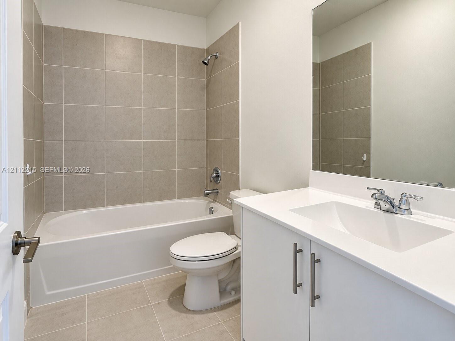 Bathroom featuring a vanity with a white countertop and integrated basin, a combination tub and shower with tile surround, and a large wall-mounted mirror