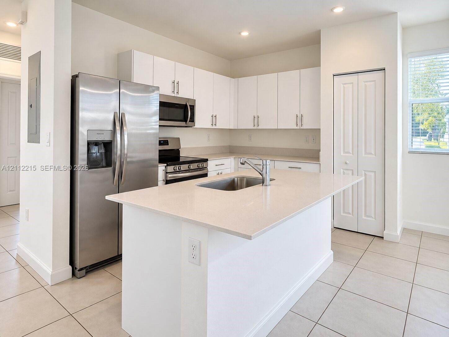 Kitchen featuring an island with a light-toned solid surface countertop, white shaker-style cabinetry, stainless steel appliances, and tile flooring