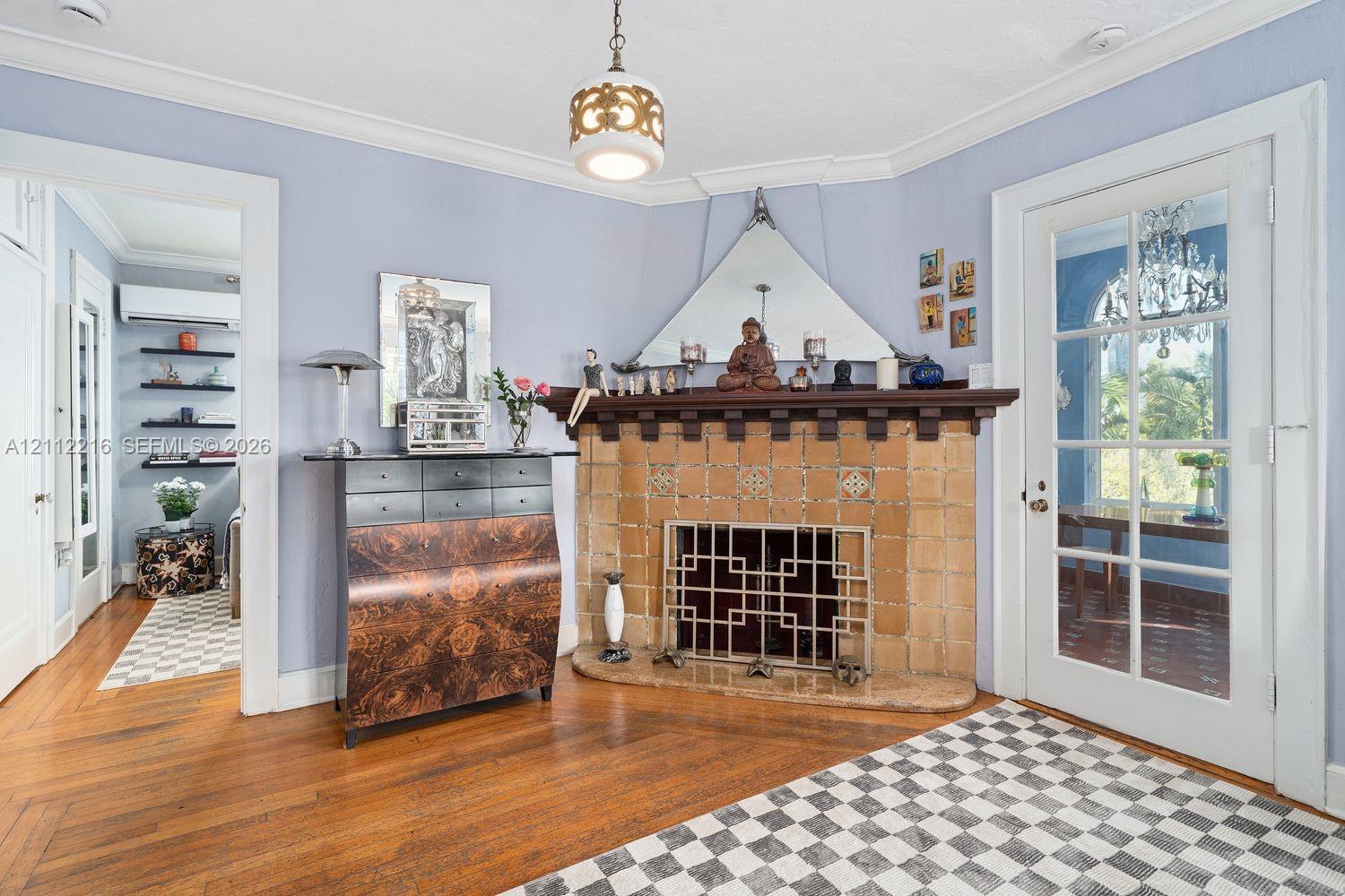 Corner fireplace featuring a detailed tile surround, dark wood mantel, and metal hearth screen, complemented by polished wood-finish flooring and a glass-paneled entry door