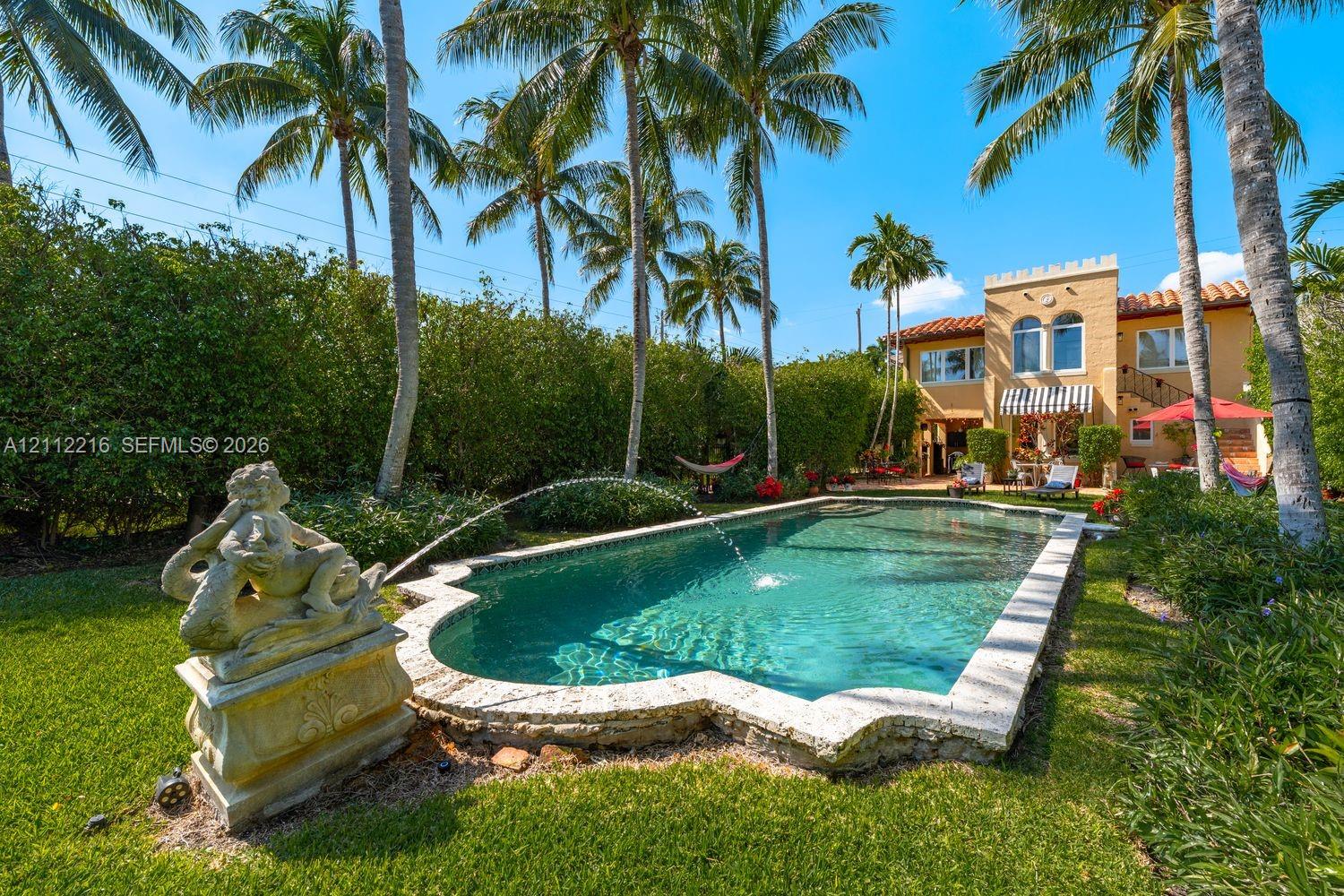 Custom-shaped swimming pool with stone coping, decorative fountain feature, and manicured lawn surrounded by mature palms