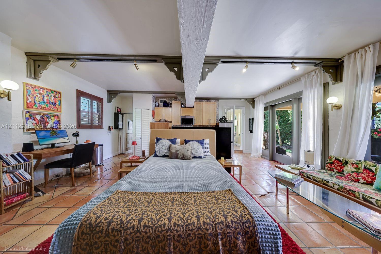 Spacious interior featuring terra cotta tile flooring, exposed structural beams with decorative corbel accents, track lighting, and sliding glass doors