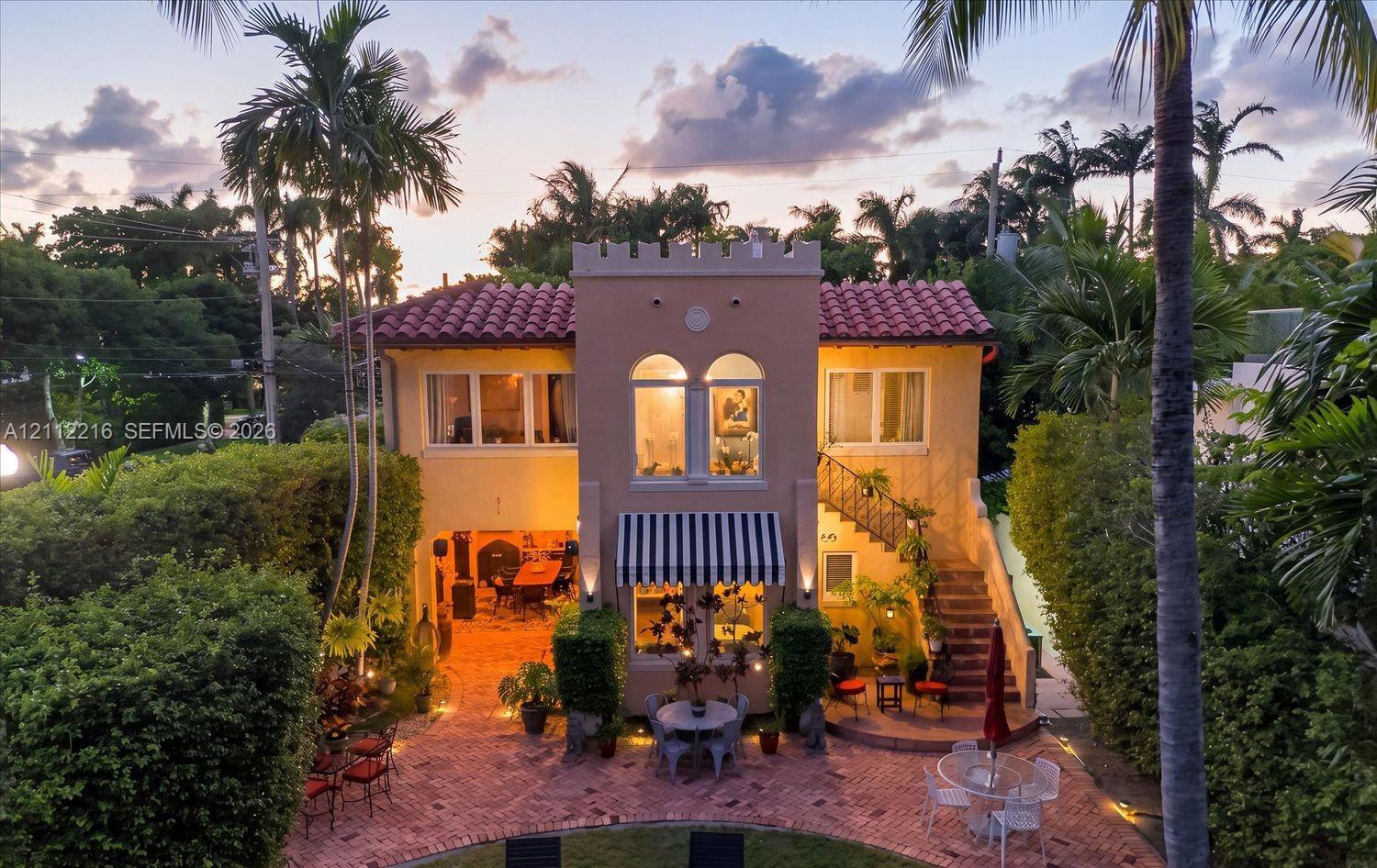 Mediterranean-style exterior featuring a terracotta tile roof, crenellated parapet, arched second-story windows, external staircase, and paved brick patio