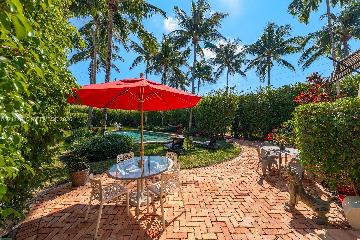 Private backyard featuring a brick patio, in-ground swimming pool, manicured landscaping, and mature palm trees