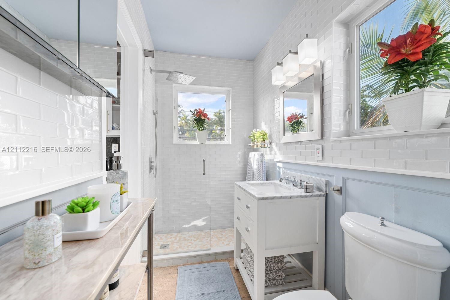 Bathroom featuring white subway tile wall cladding, a walk-in shower with a rainfall showerhead, a freestanding vanity with a stone countertop, and polished chrome light fixtures