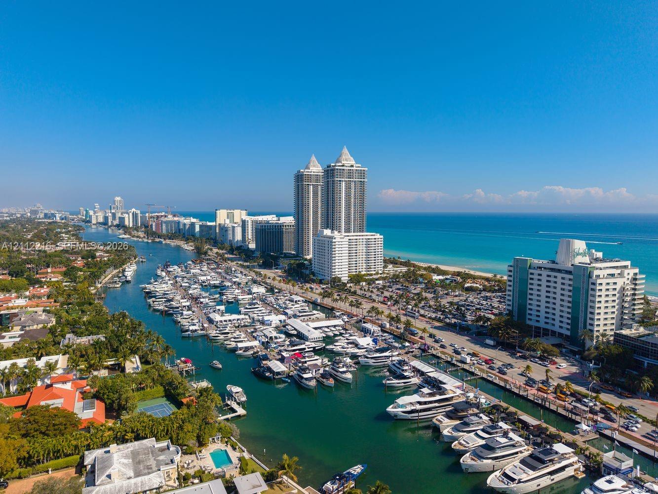 Aerial perspective of coastal landscape featuring a deep-water marina, ocean coastline, expansive high-rise structures, and residential properties with private swimming pools