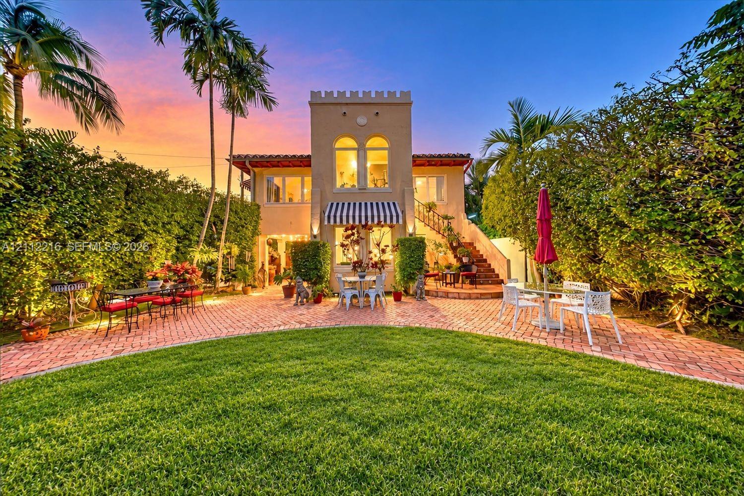 Mediterranean-inspired exterior featuring a crenelated roofline, brick paver patio, arched window detailing, exterior masonry staircase, and a manicured lawn