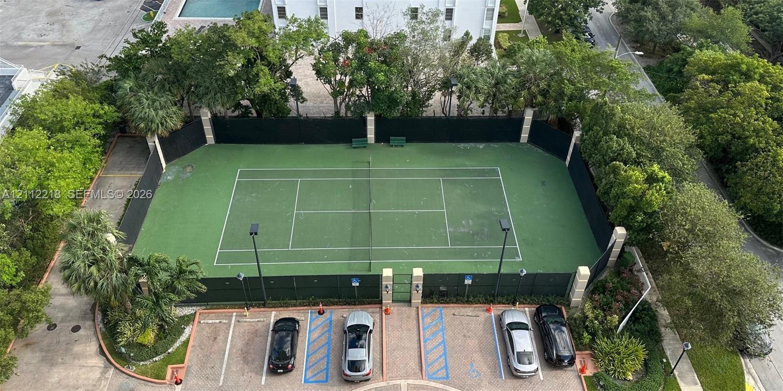 Private tennis court featuring a fenced perimeter, outdoor lighting, and paved parking area