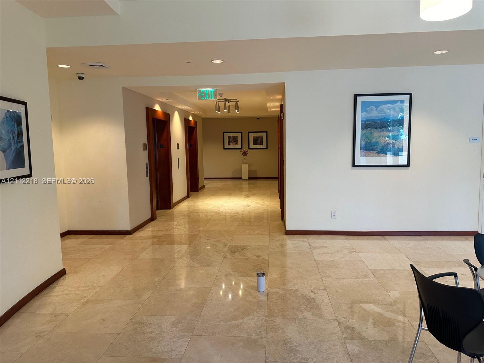 Large-format stone flooring throughout the common area, recessed ceiling lighting, and wood-trim elevator surrounds