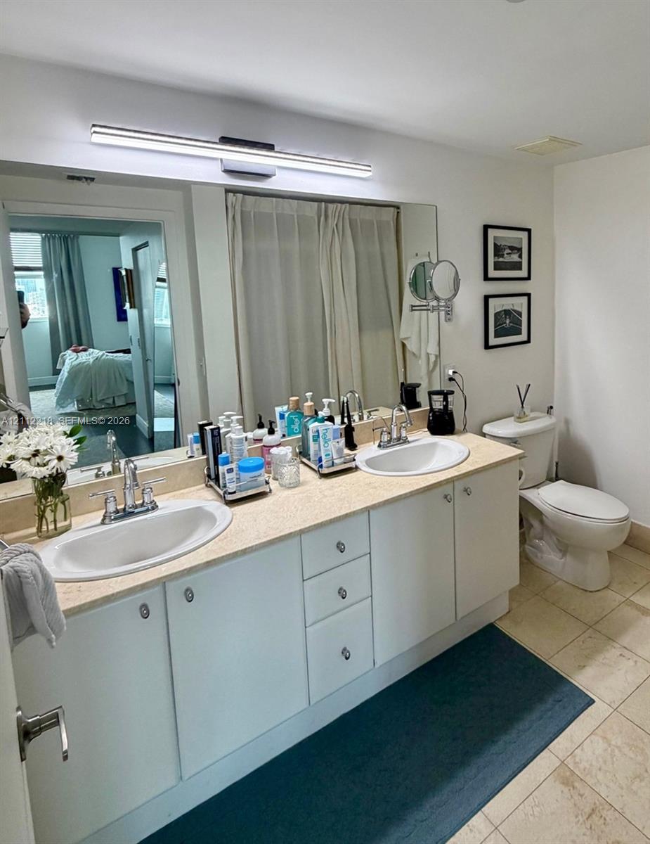 Dual-sink vanity with a solid-surface countertop, integrated oval basins, chrome-finish dual-handle faucets, and a full-width wall mirror with integrated LED light fixture