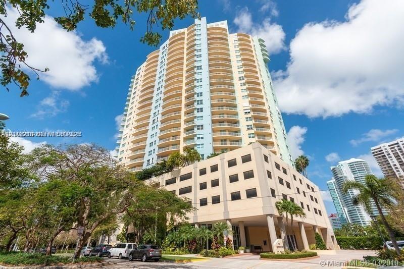 High-rise residential tower featuring tiered balconies, a structured parking podium, concrete exterior, and a porte-cochre entry