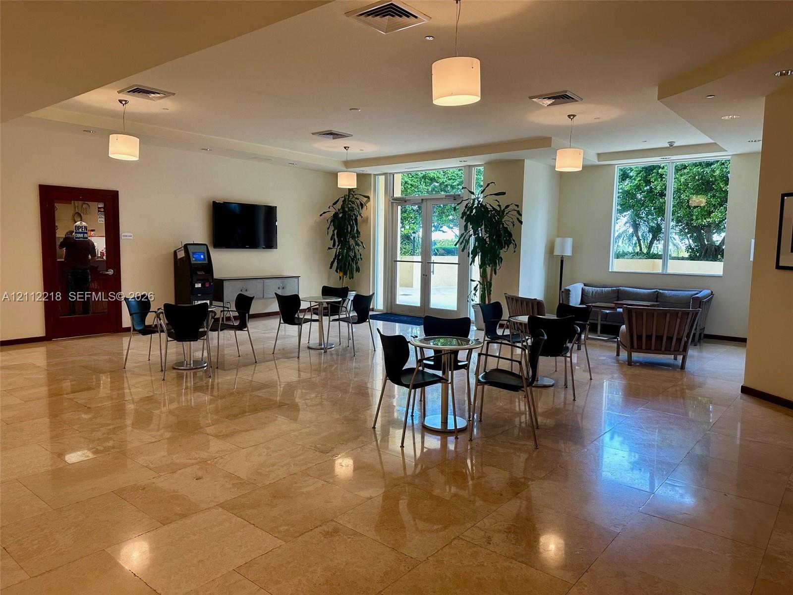 Open-concept lounge featuring polished stone flooring, recessed lighting, neutral wall tones, and glass-paneled double door entry