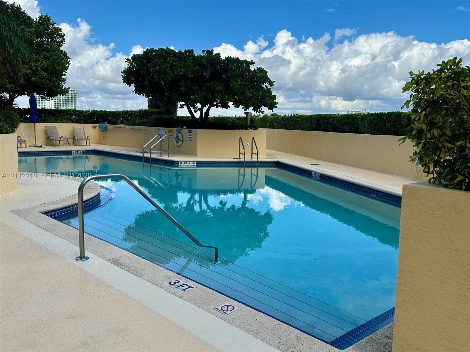 Swimming pool featuring integrated stairs, metal handrails, a perimeter tiled edge, and a surrounding concrete deck