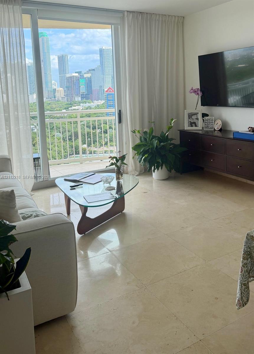 Floor-to-ceiling sliding glass doors opening to a balcony with metal railings and expansive city skyline scenery, complemented by large-format light-toned stone flooring
