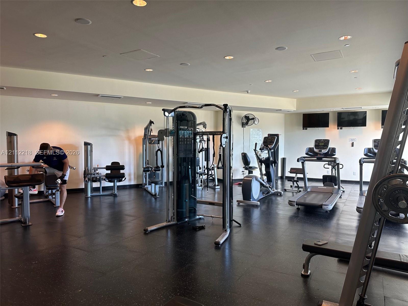 Fitness center featuring recessed lighting, dark composite flooring, and wall-mounted television screens