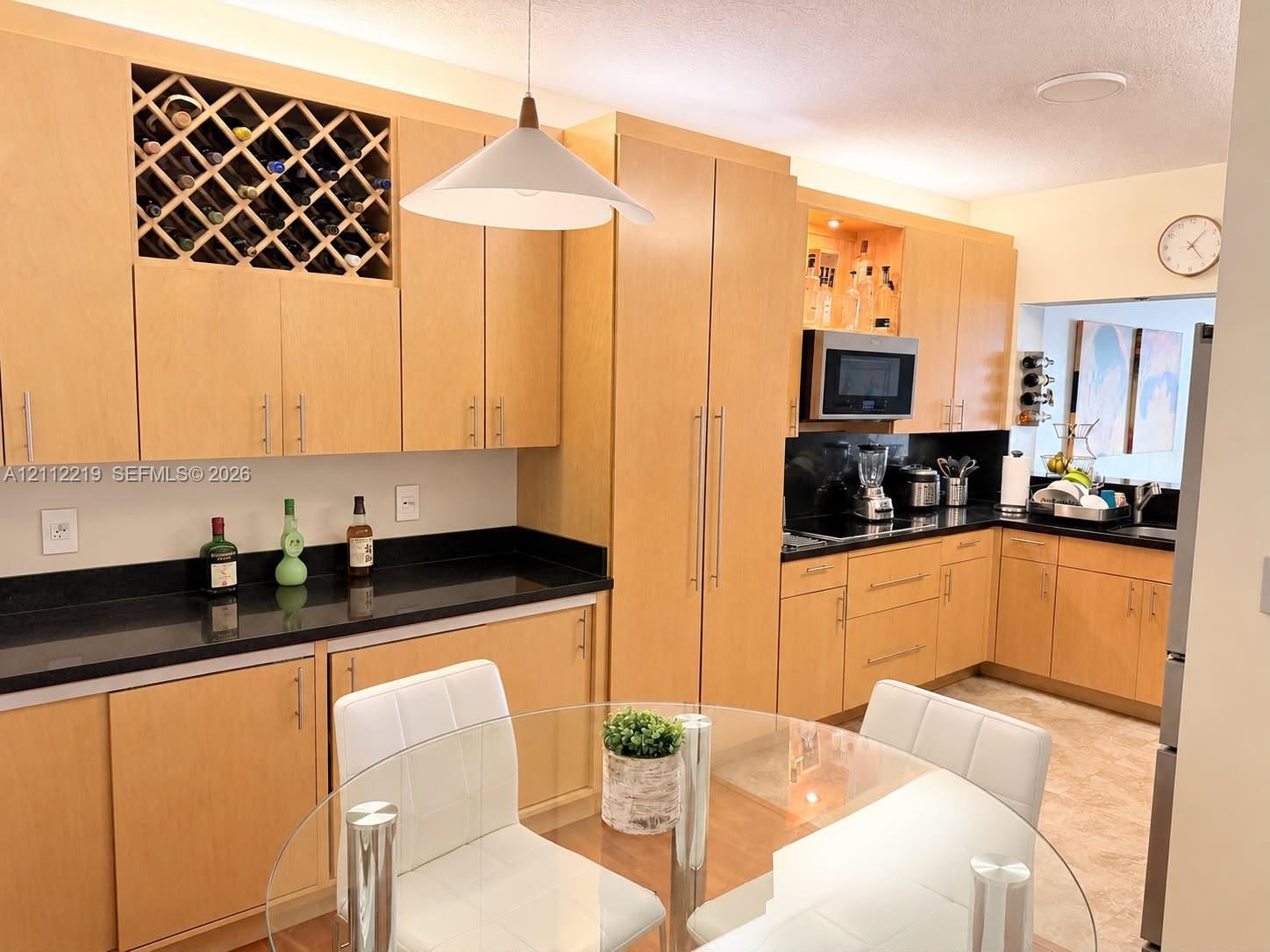 Light-finish cabinetry featuring built-in wine storage, dark solid-surface countertops, and an integrated microwave