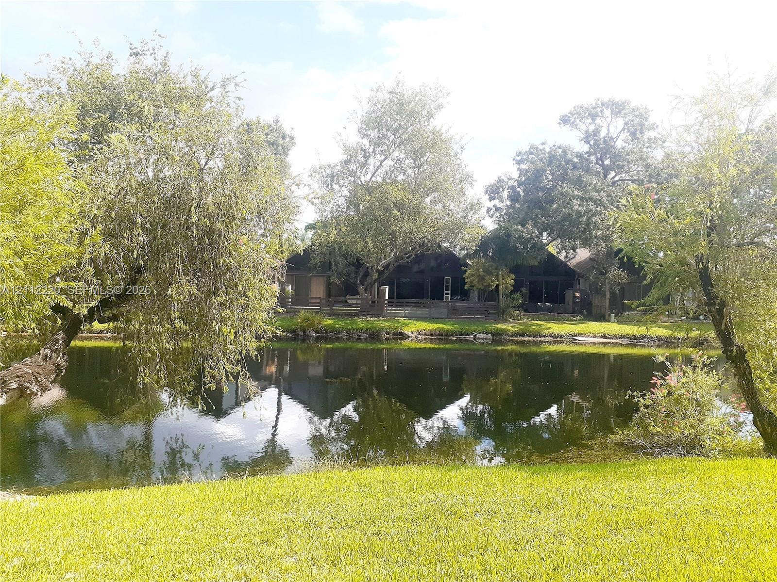Waterfront property featuring a manicured lawn, mature trees, and a screened-in porch