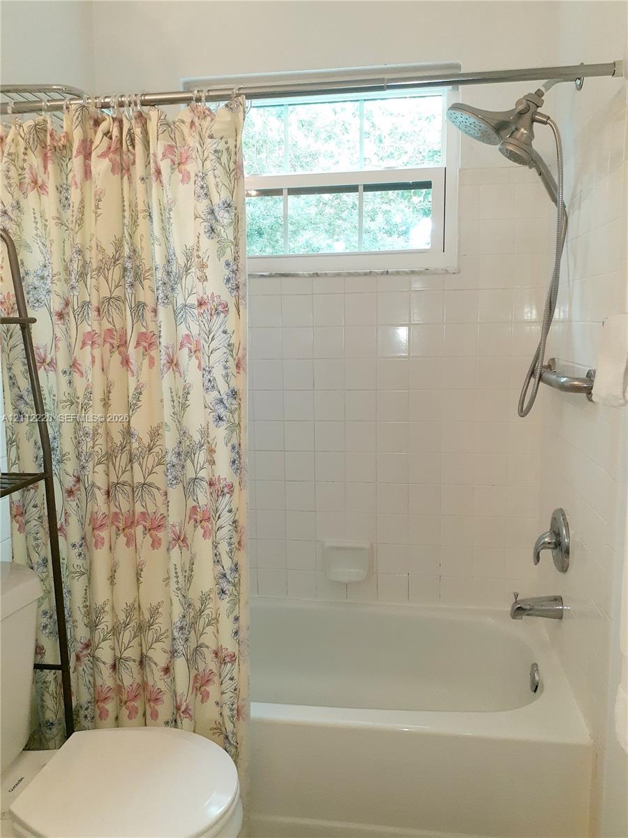 Bathtub and shower combination featuring white tiled wall surround, stainless steel dual shower head fixture, and built-in recessed soap dish
