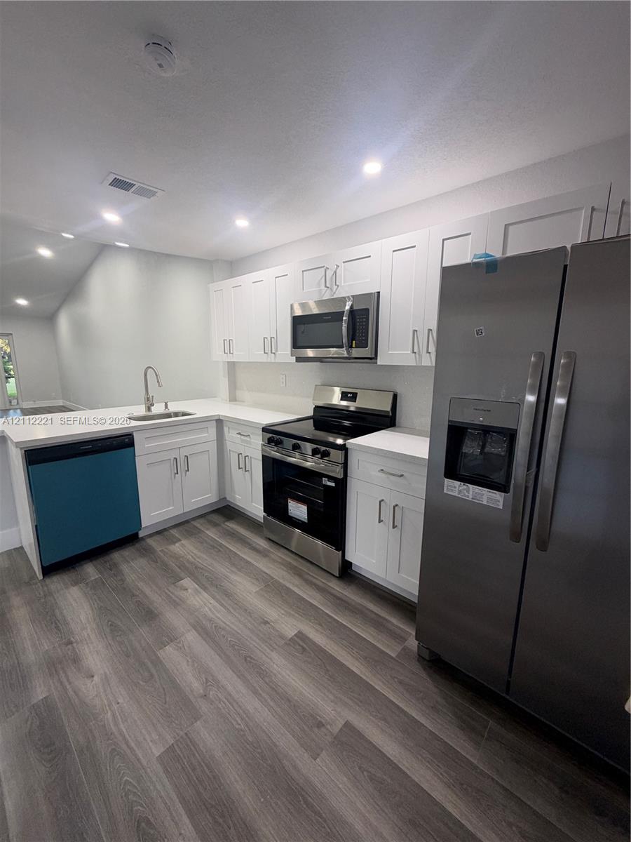 Kitchen featuring white shaker-style cabinetry, solid-surface countertops, wood-finish flooring, and stainless steel appliances Kitchen featuring white shaker-style cabinetry, solid-surface countertops, wood-finish flooring, and stainless steel appliances