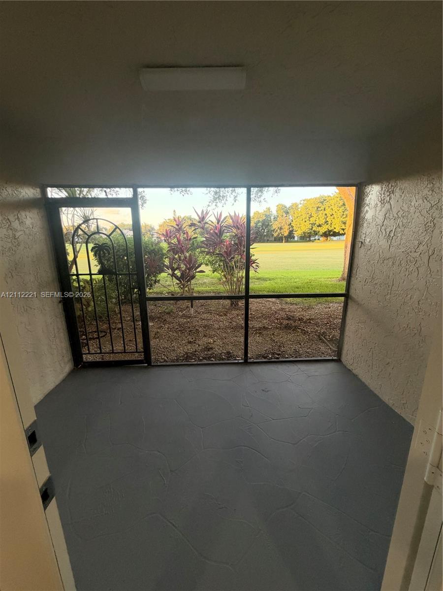 Screen-enclosed porch with textured gray concrete flooring, decorative metal security door, and exterior stucco walls Screen-enclosed porch with textured gray concrete flooring, decorative metal security door, and exterior stucco walls