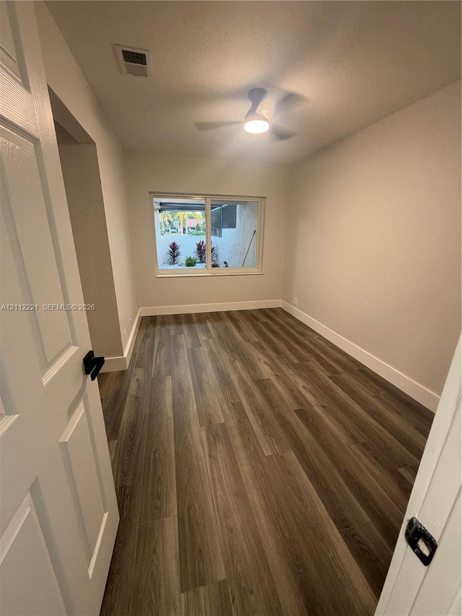 Neutral-toned interior featuring wood-finish flooring, a sliding window with exterior hardscaping, and a ceiling-mounted light fixture Neutral-toned interior featuring wood-finish flooring, a sliding window with exterior hardscaping, and a ceiling-mounted light fixture