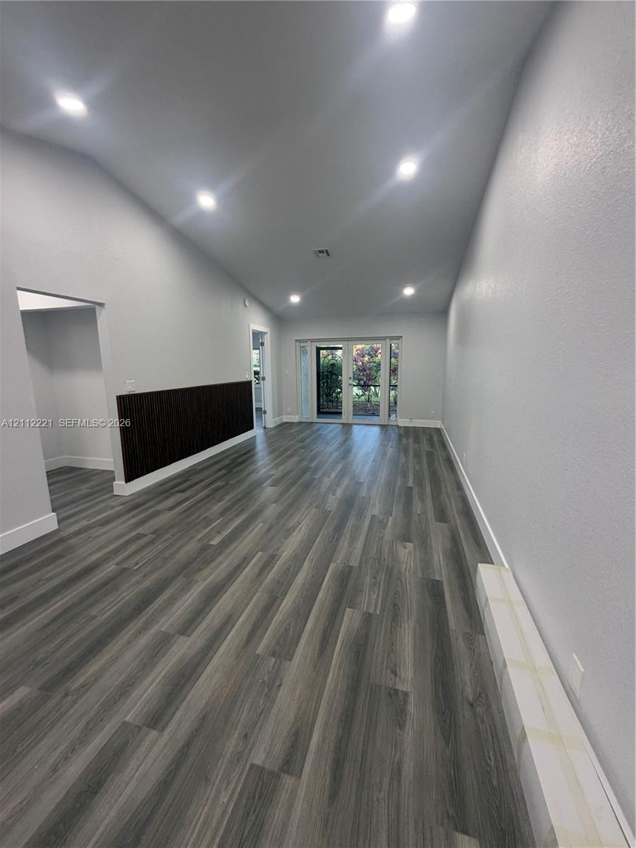 Interior space featuring a vaulted ceiling, wood-finish flooring, recessed lighting, and a dark-toned vertical slat accent wall Interior space featuring a vaulted ceiling, wood-finish flooring, recessed lighting, and a dark-toned vertical slat accent wall