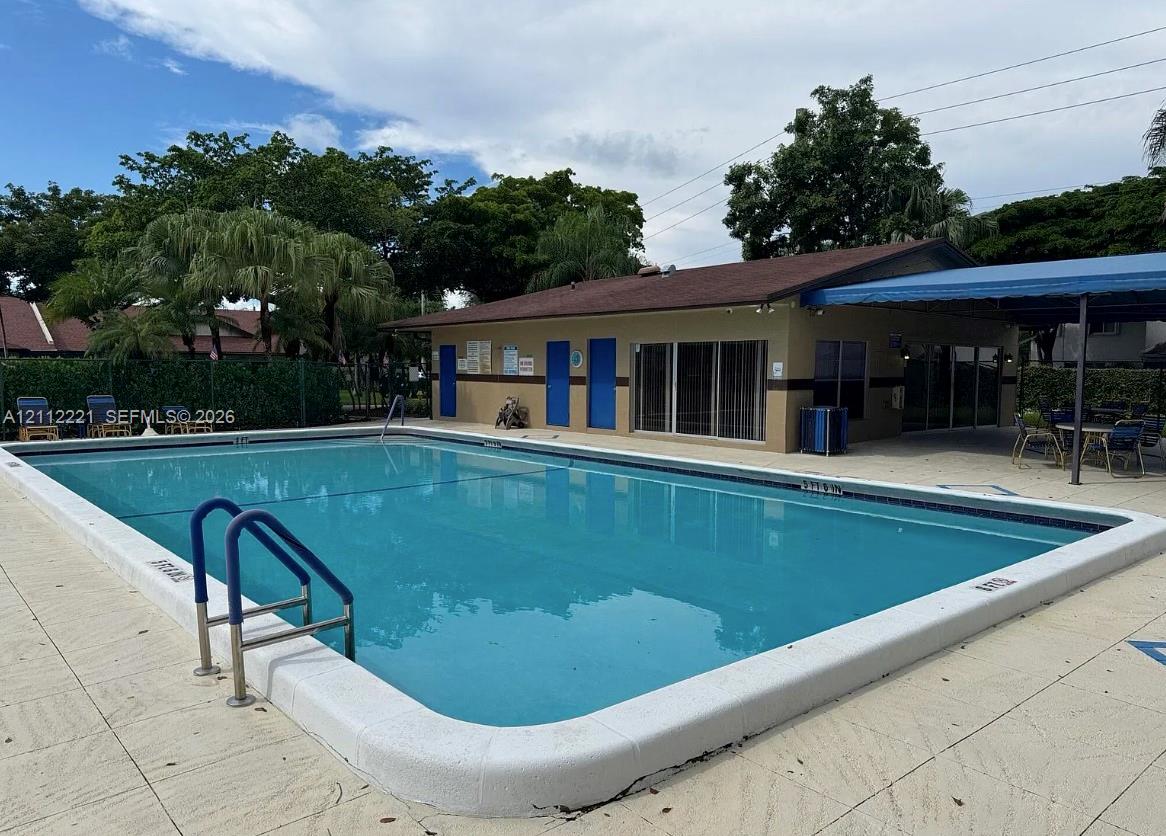 In-ground swimming pool featuring a concrete deck, metal handrails, and a covered patio area
