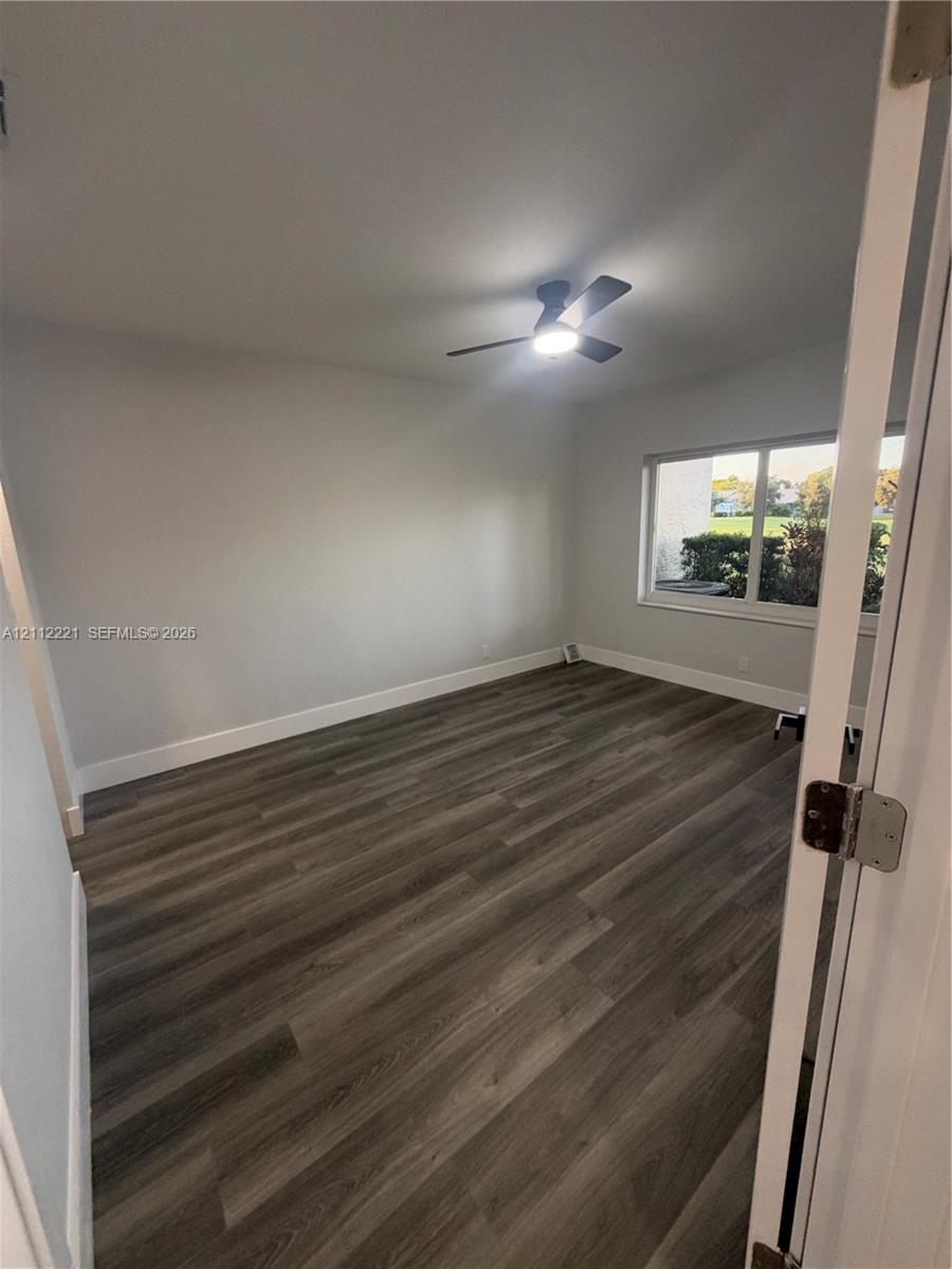 Neutral interior space featuring wood-finish flooring, a ceiling fan with integrated lighting, and a large window Neutral interior space featuring wood-finish flooring, a ceiling fan with integrated lighting, and a large window