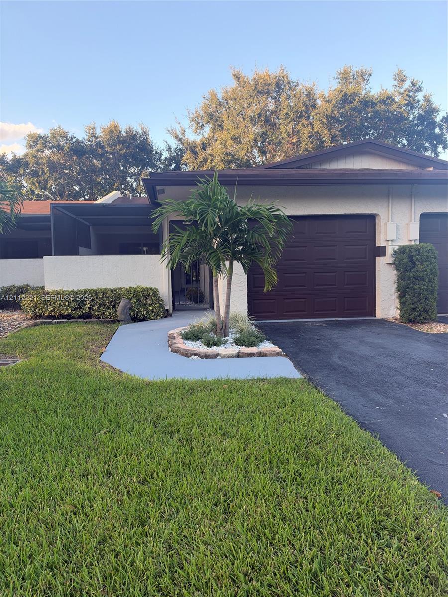 Single-story stucco exterior featuring a paneled garage door, a painted concrete walkway, and a landscaped planter bed with a palm tree