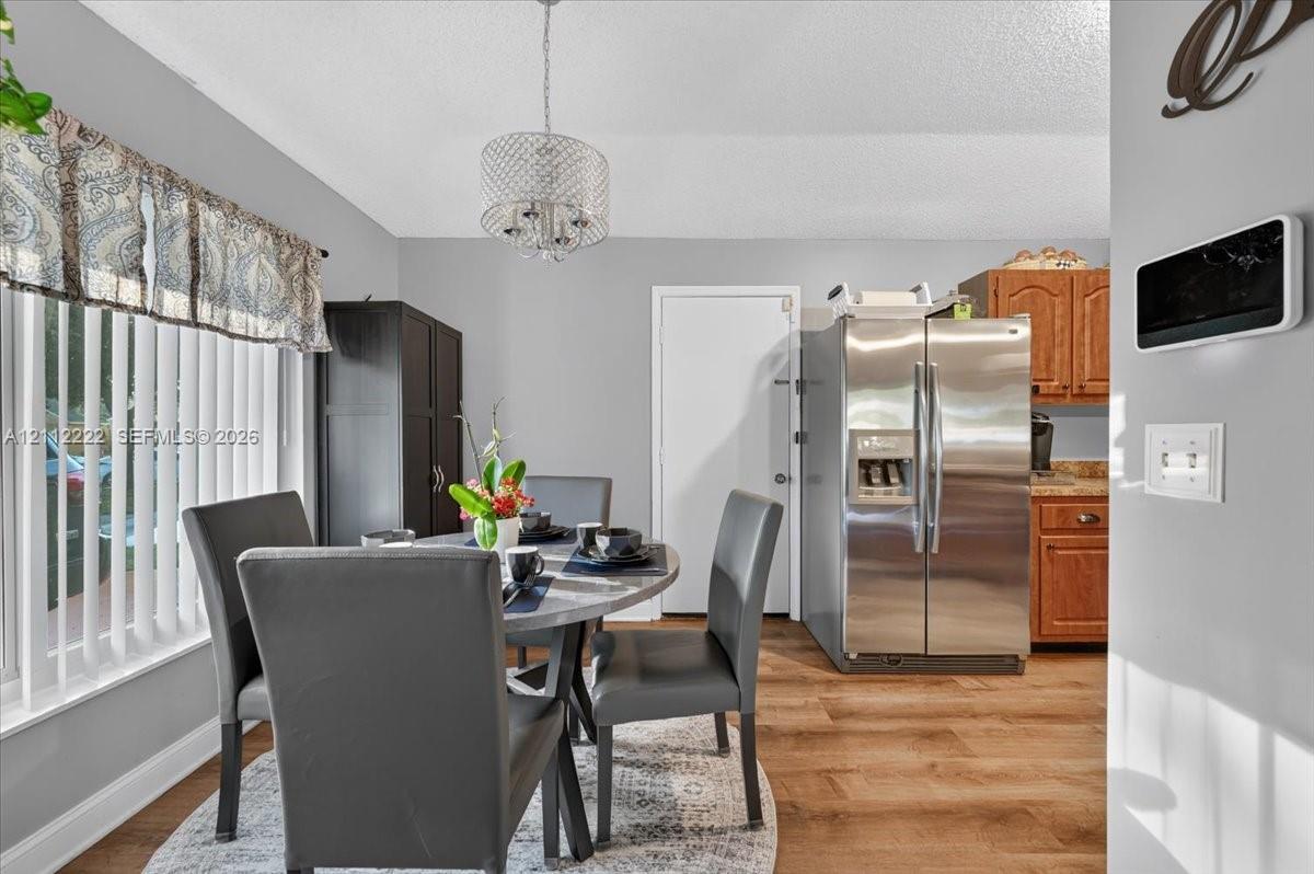 Wood-finish flooring, stainless steel side-by-side refrigerator, crown-molded drum pendant lighting, and vertical window blinds