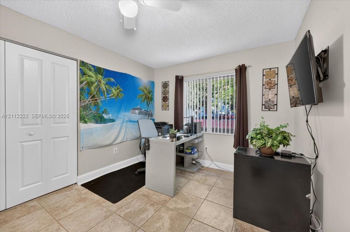 Room featuring neutral-toned tile flooring, dual-panel closet doors, vertical window blinds, and a ceiling-mounted light fixture