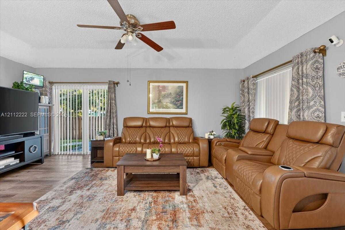 Living area featuring tray ceilings, wood-finish flooring, and sliding glass doors with vertical blinds
