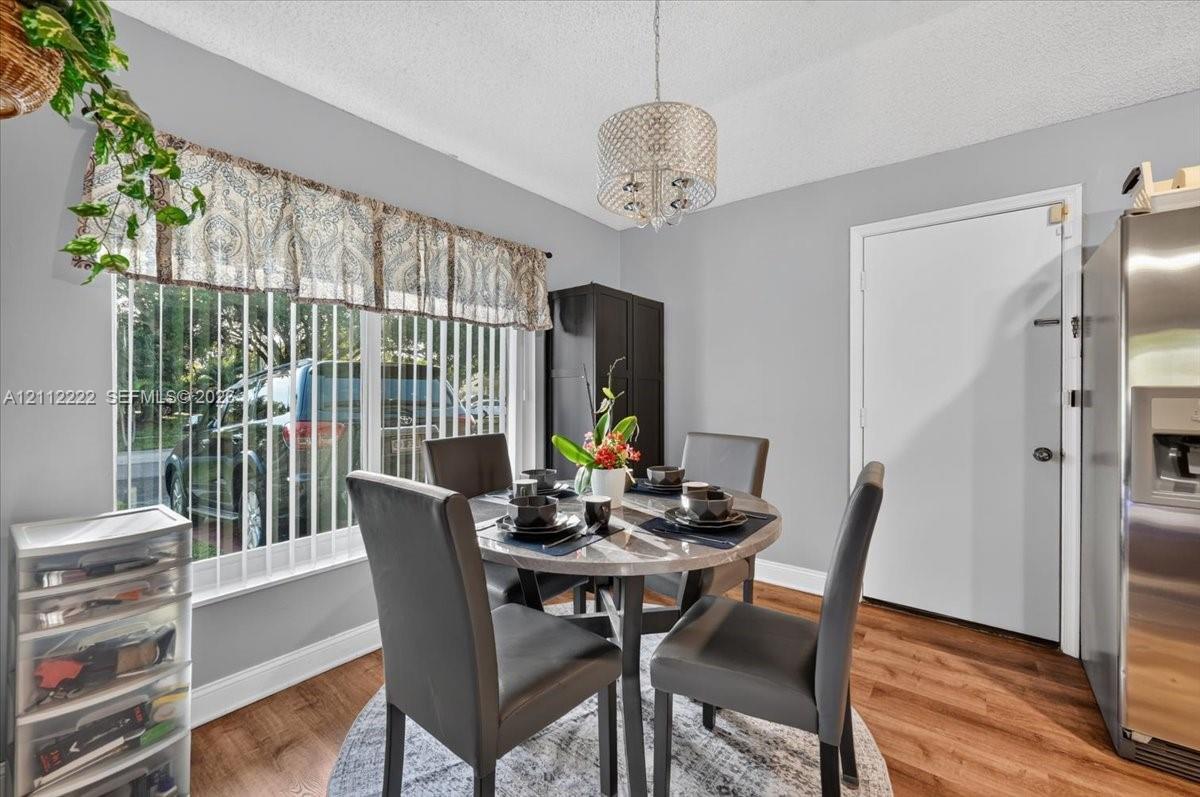 Dining area featuring wood-finish flooring, a decorative drum-style chandelier, and a large window with vertical blinds