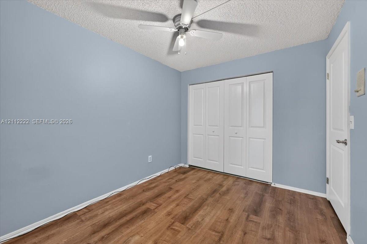 Room featuring wood-finish flooring, a ceiling fan with integrated lighting, textured ceiling, and a four-panel bi-fold closet