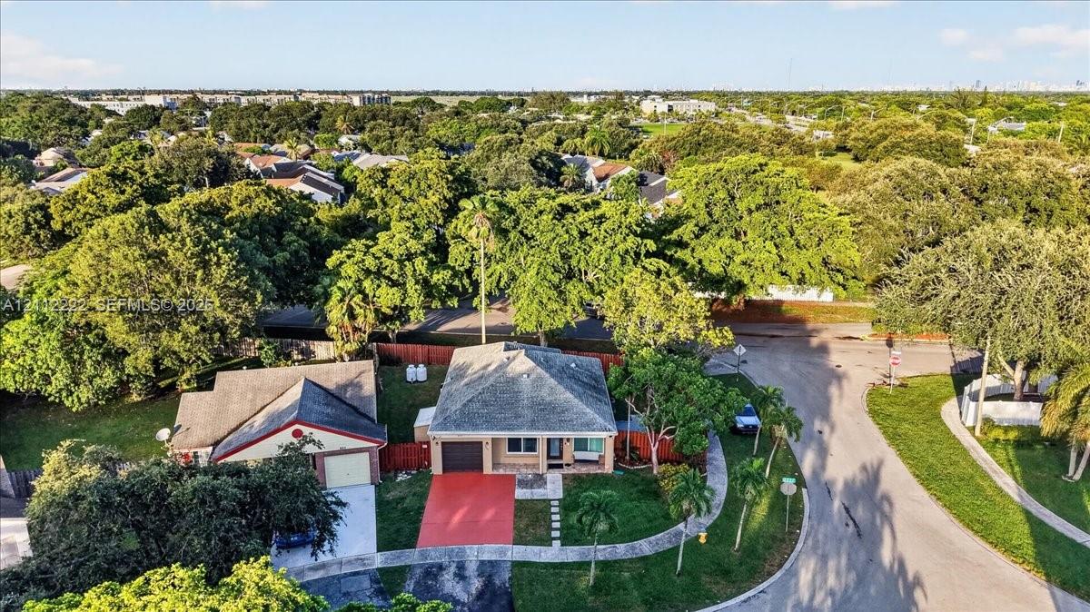 Aerial perspective of a detached residence featuring a multi-hipped roofline, concrete driveway, attached garage, and mature tree-lined landscaping