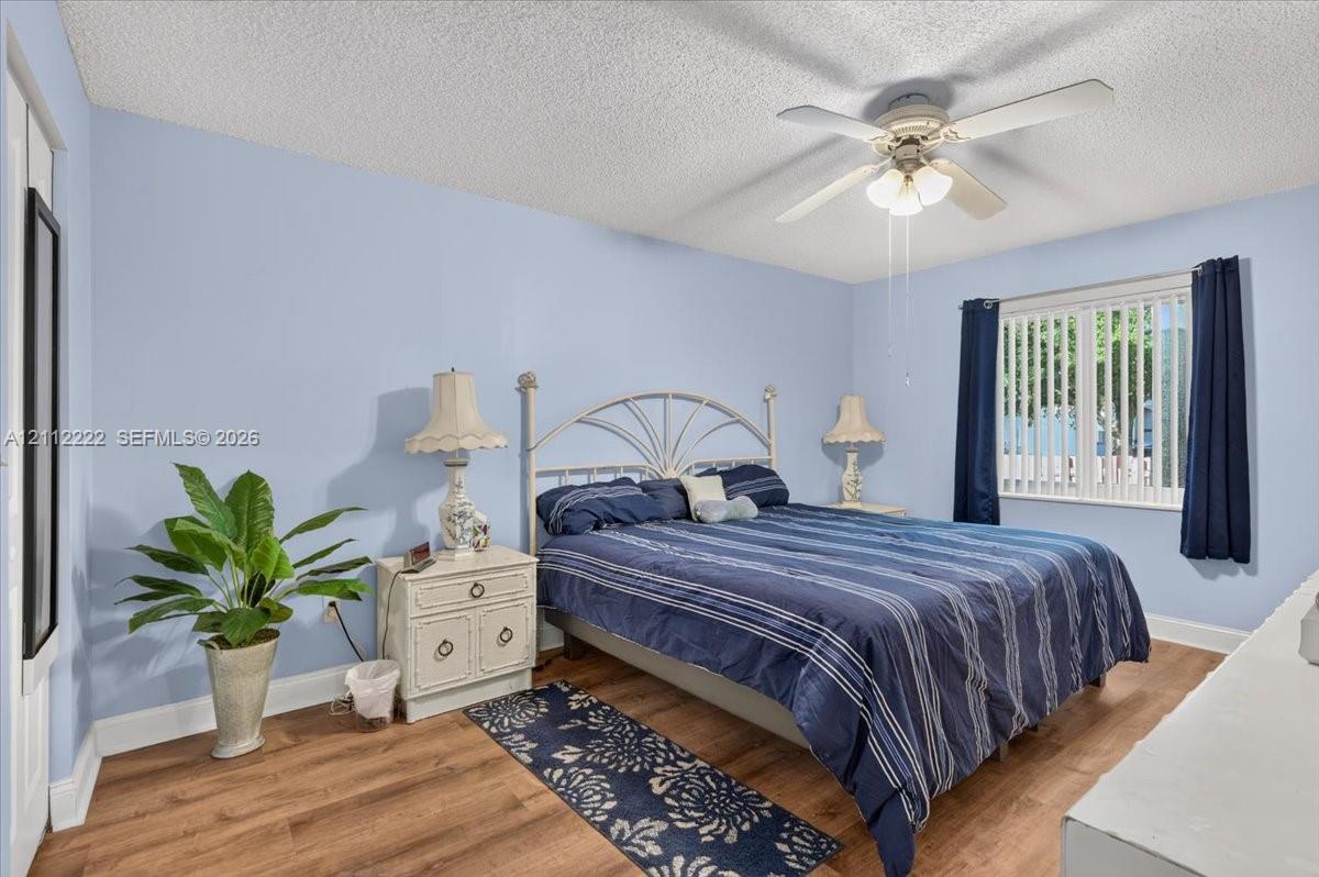 Bedroom featuring wood-finish flooring, a ceiling fan with integrated lighting, and a window with vertical blinds