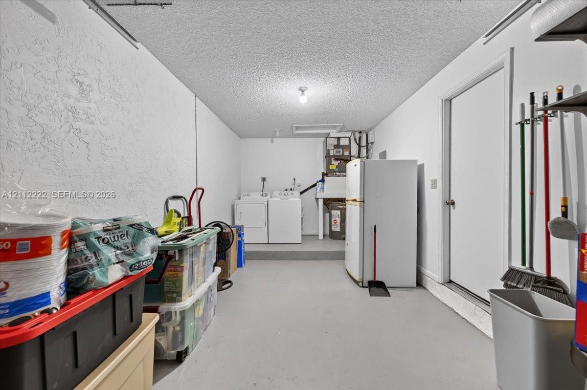 Utility space featuring painted concrete flooring, textured walls, a ceiling-mounted light fixture, and a built-in utility sink