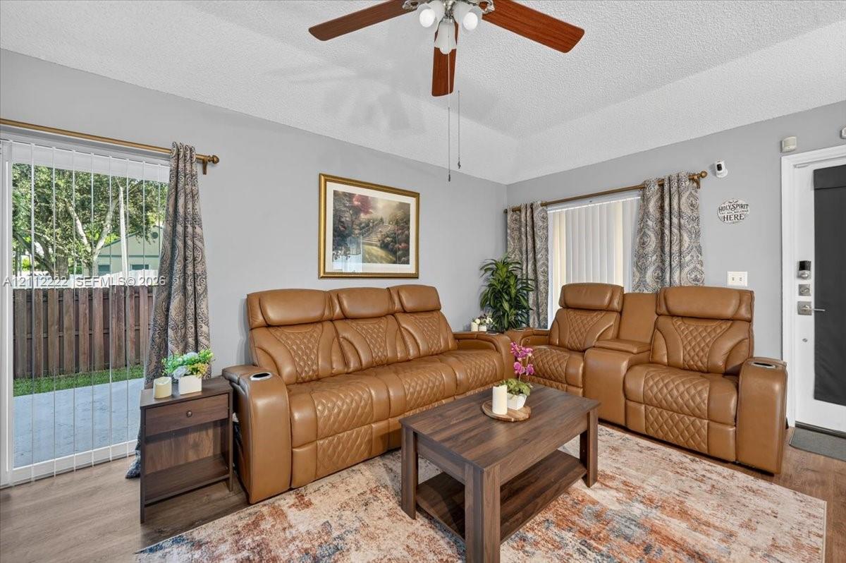 Living space featuring a tray ceiling, ceiling fan with light fixture, wood-finish flooring, and sliding glass doors with access to an exterior concrete patio