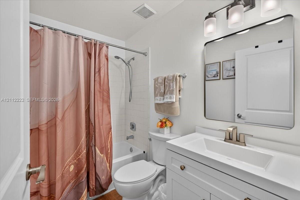 Bathroom featuring a white vanity with an integrated rectangular sink, a rectangular mirror with rounded corners, a three-light fixture, and a tub-shower combination with white subway-style wall tiling